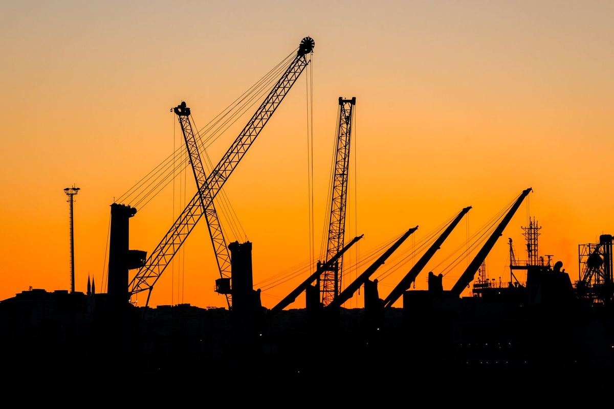 Construction cranes silhouetted at sunset